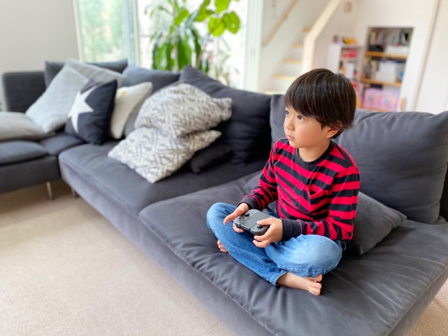 自宅のソファーに座ってテレビゲームをする男の子