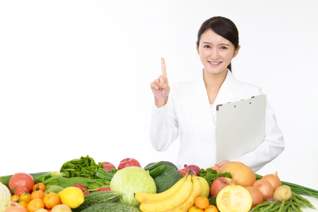野菜やくだものの後ろに栄養士の女性がいる写真
